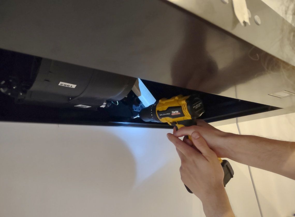 Using a yellow electric screwdriver on a black cooker hood