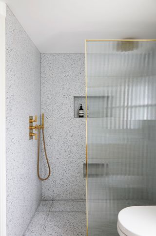 a wet room with large terrazzo tiles and a reeded glass shower screen