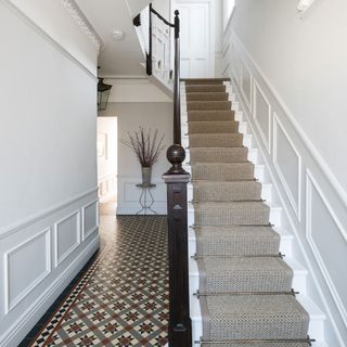 hallway with white wall staircase with rug designed flooring