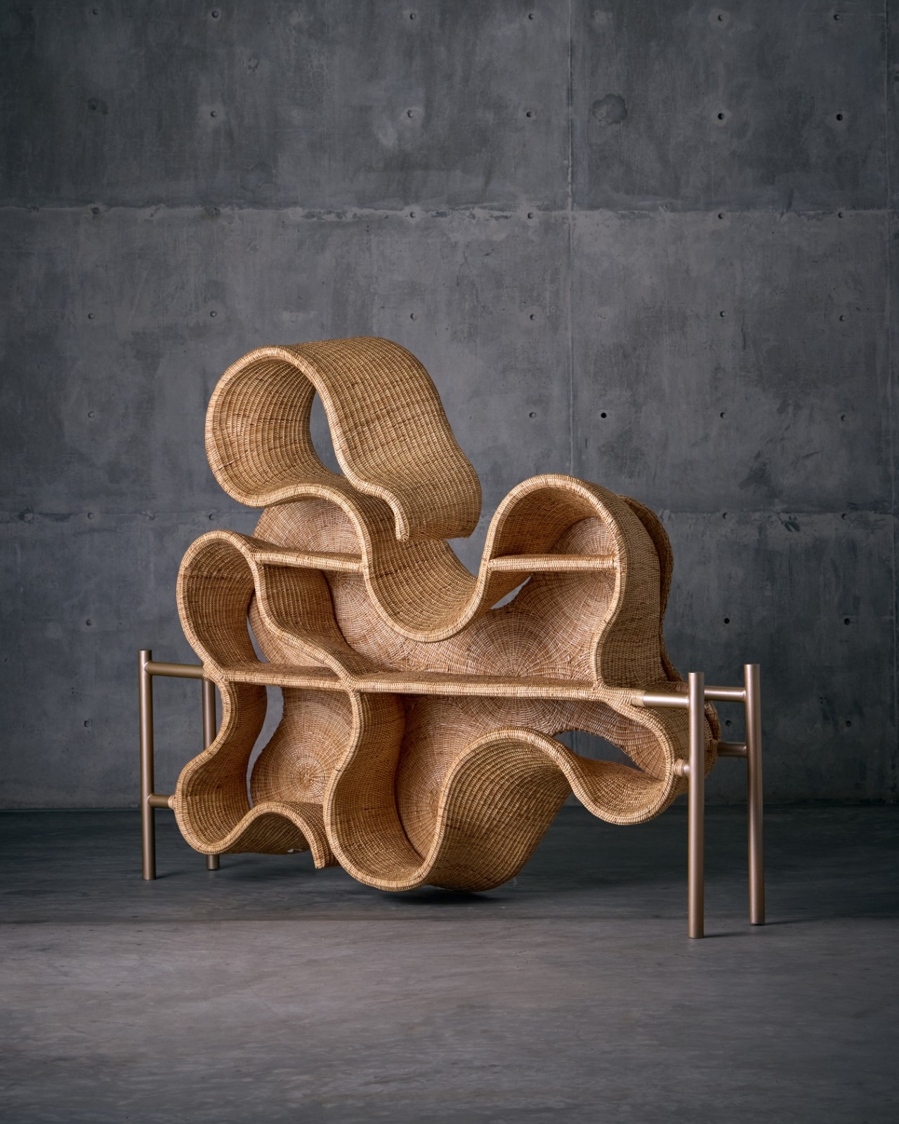 A large-scale, wiggly, wicker shelving unit against a cement wall and pavement.