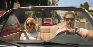 Miranda (Elen Rhys) and Max (Julian Looman) are in an open-topped car driving through the streets of Mallorca with. Max at the wheel