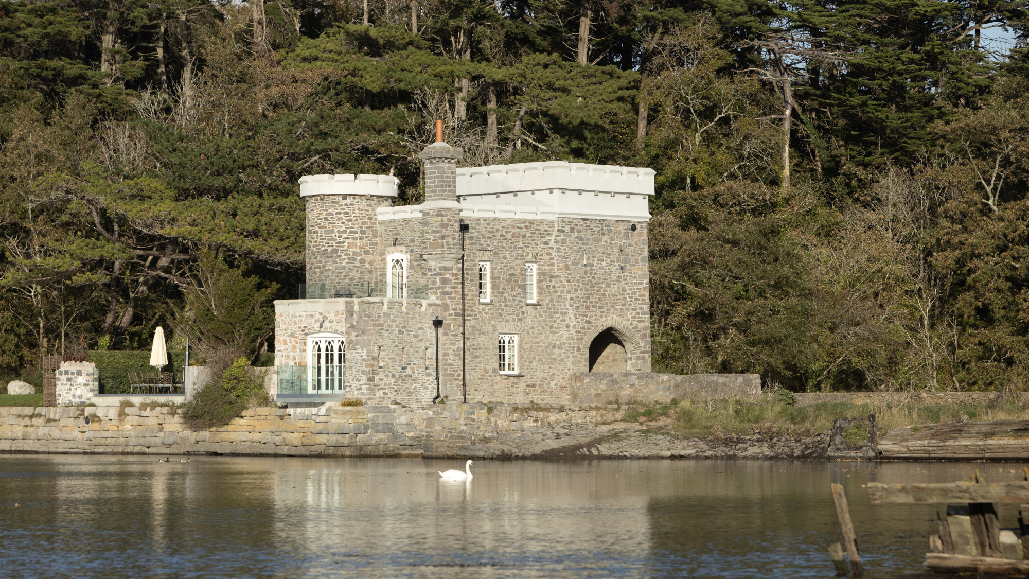 Exterior of castle-style home beside a lake with trees behind it