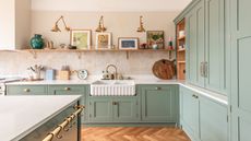 A sage green kitchen with brass gold handle. There is a belfast sink with a gold tap and gold light fixtures placed above the sink.