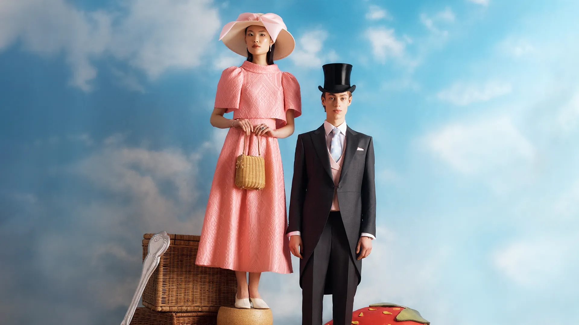 Woman in a pink dress and man in a morning suit posing next to a picnic hamper
