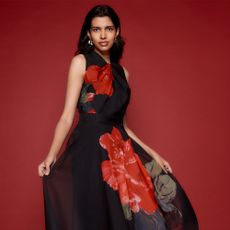 Model on a red background wearing a floral dress sold at Phase Eight