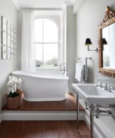 An example of how to make a small bathroom look bigger showing a small freestanding bath beneath a window on a wooden floor