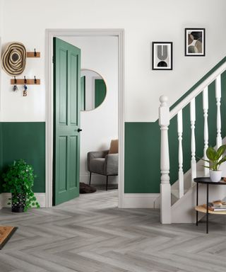 A hallway with white and green walls, a green door, black and white wall art, a white staircase, and gray wooden vinyl flooring