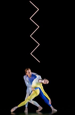 Male and female ballet dancers doing a duet on stage wearing blue and yellow unitards