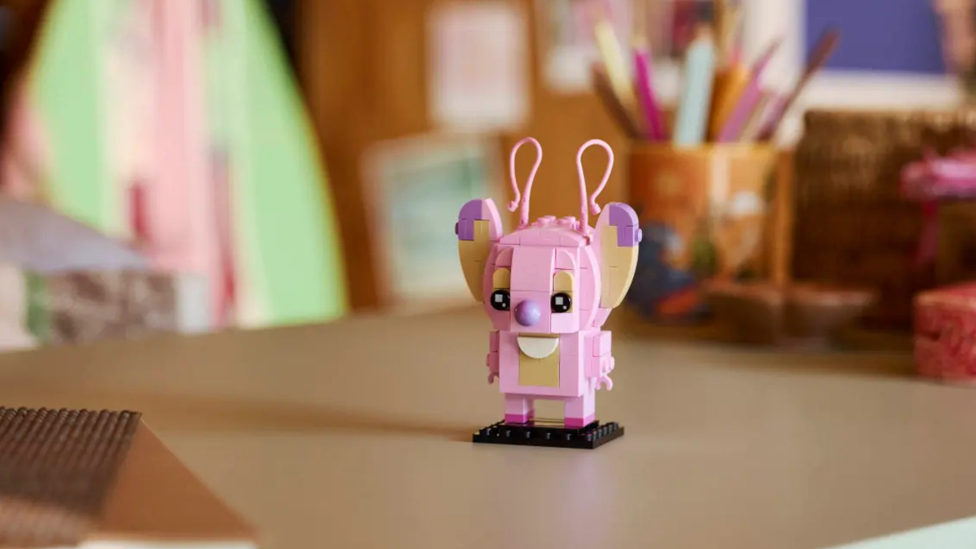 Lego Angel BrickHeadz figure on a wooden surface, with pencils in a pencil pot visible in the distance