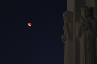 The partially eclipsed moon is visible behind a statue at the entrance to the Griffith Observatory in Los Angeles.