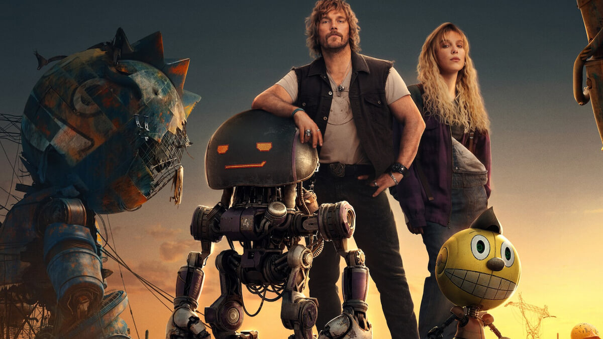 Two humans stand with three goofy-looking sci-fi robots