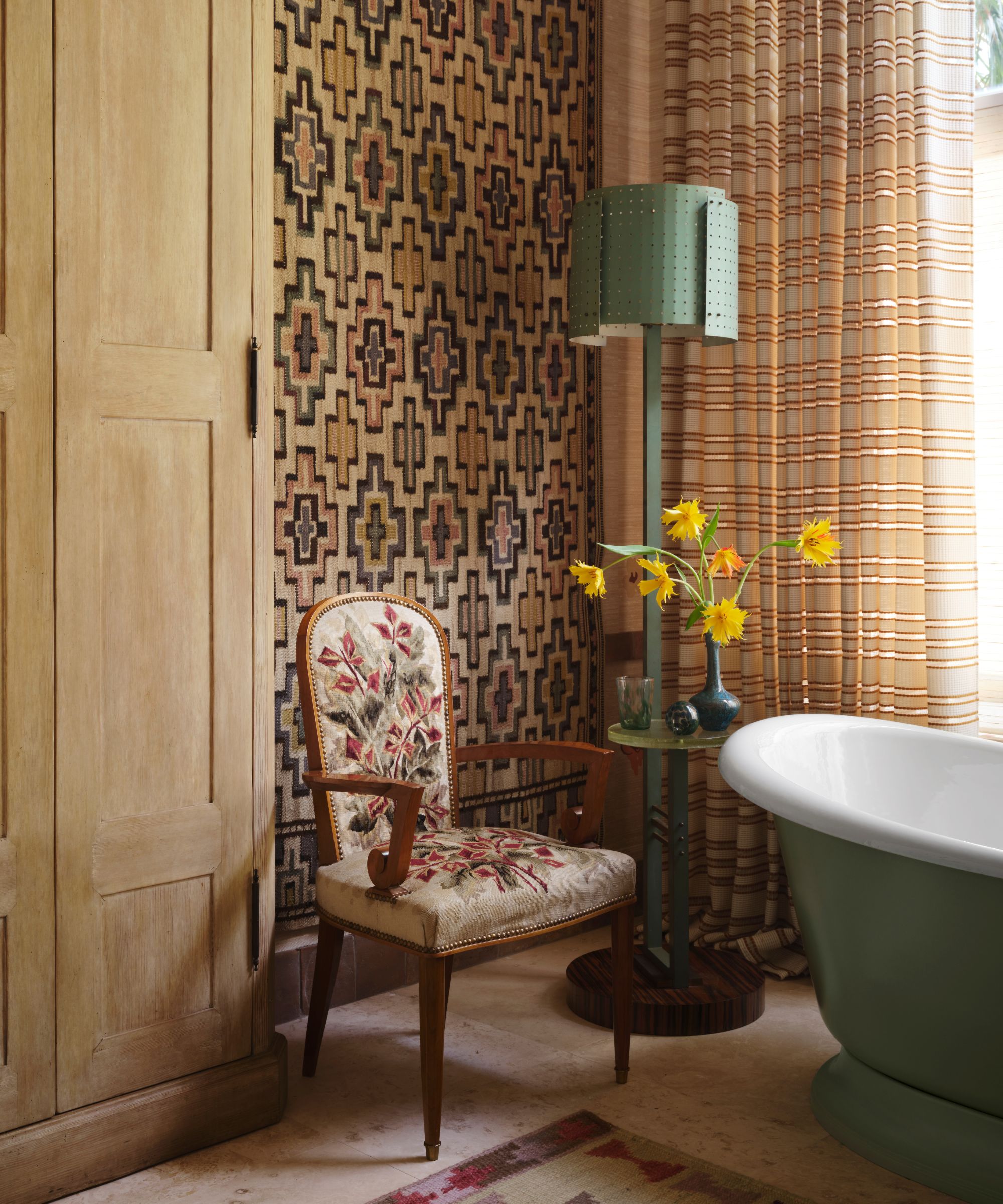 A luxury bathroom featuring a green clawfoot-style tub, a geometric wall tapestry, and an antique floral chair
