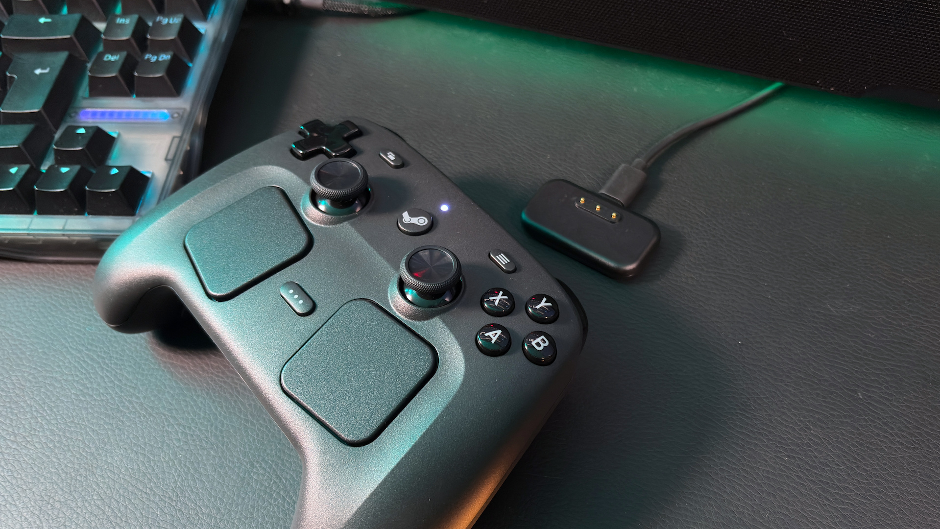 The Steam Controller on a desk next to its charging dock and a keyboard.