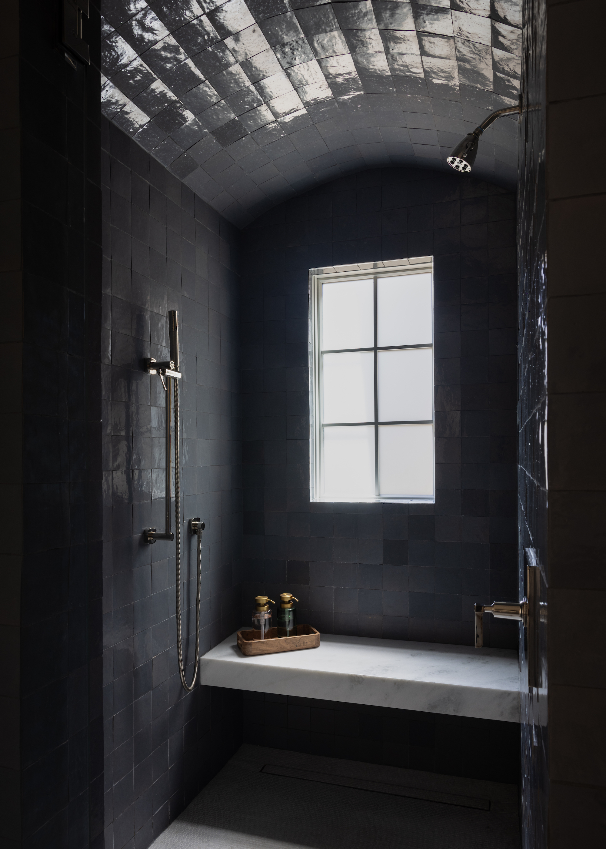 bathroom with black zellige tiles in a shower room. There is also a seat in the shower room with two soap pumps.