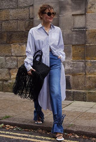 a woman's shirtdress outfit with striped dress styled over jeans with tie-up sandals and fringe tote bag