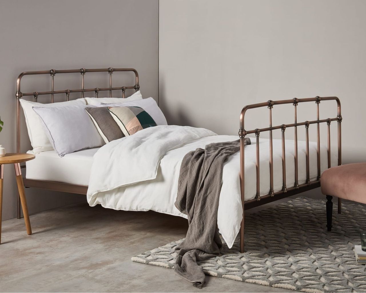 Brass bed frame in grey room with white duvet covers, pink velvet chair and geometric rug