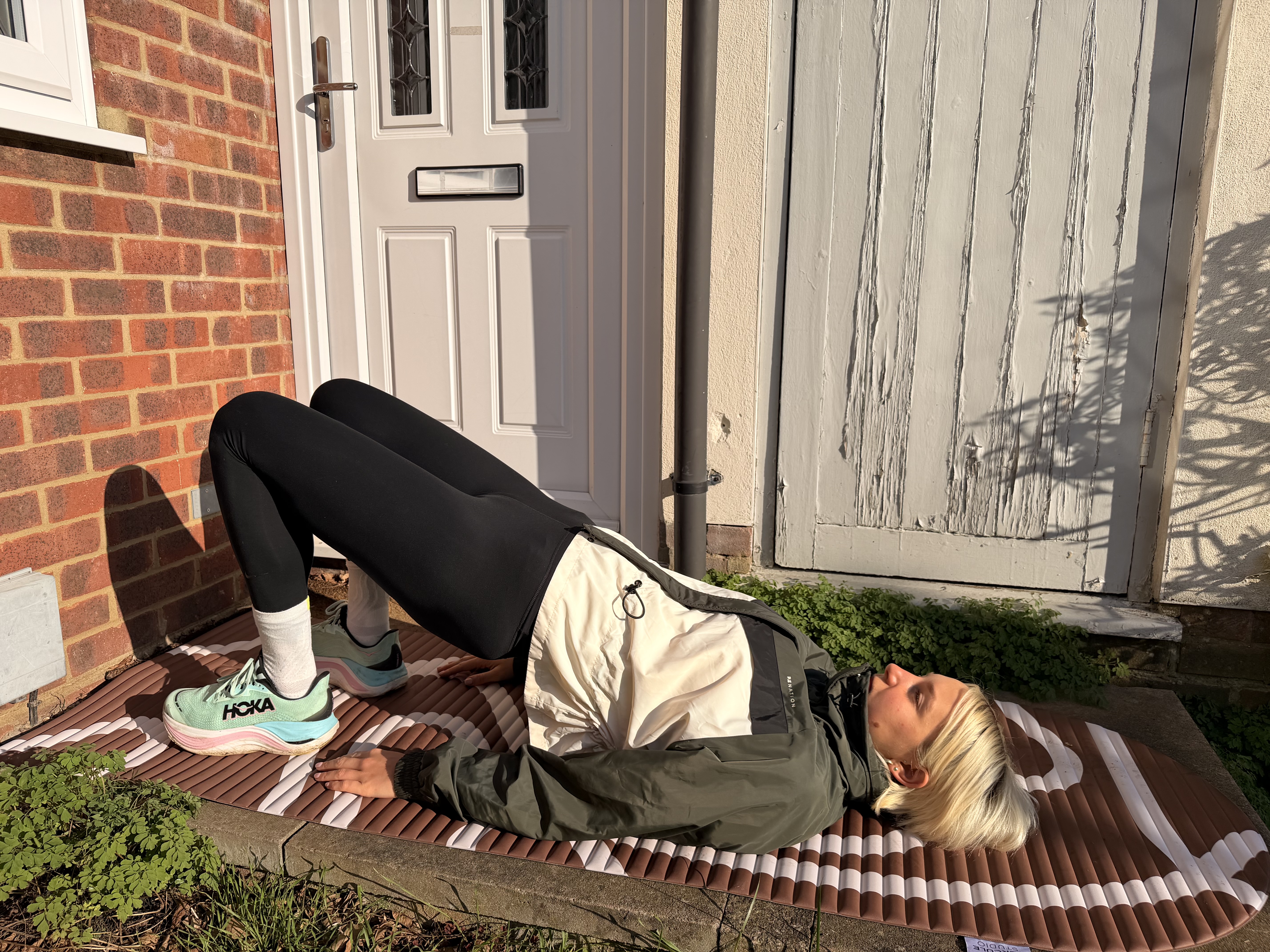 A woman lying on the ground in running clothes with her hips raised and feet flat on the floor