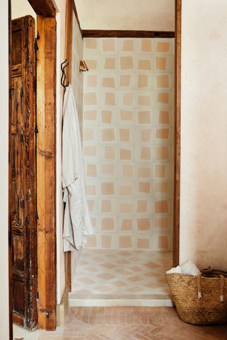 A shower with geometric pink and white tiles, a woven basket and brass shower head