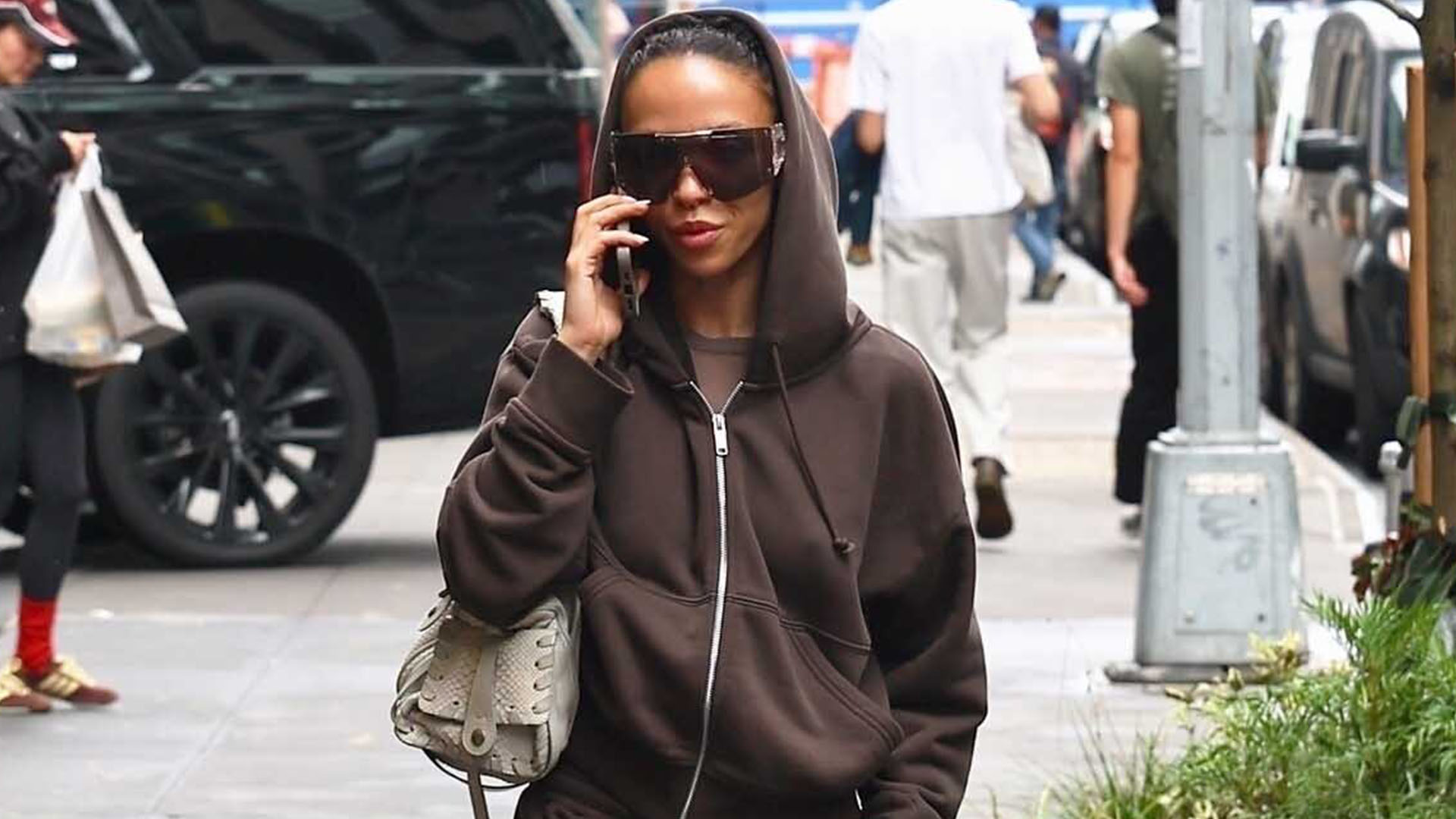 FKA Twigs wearing a brown hoodie, brown Bermuda shorts, brown boots, a gray shoulder bag