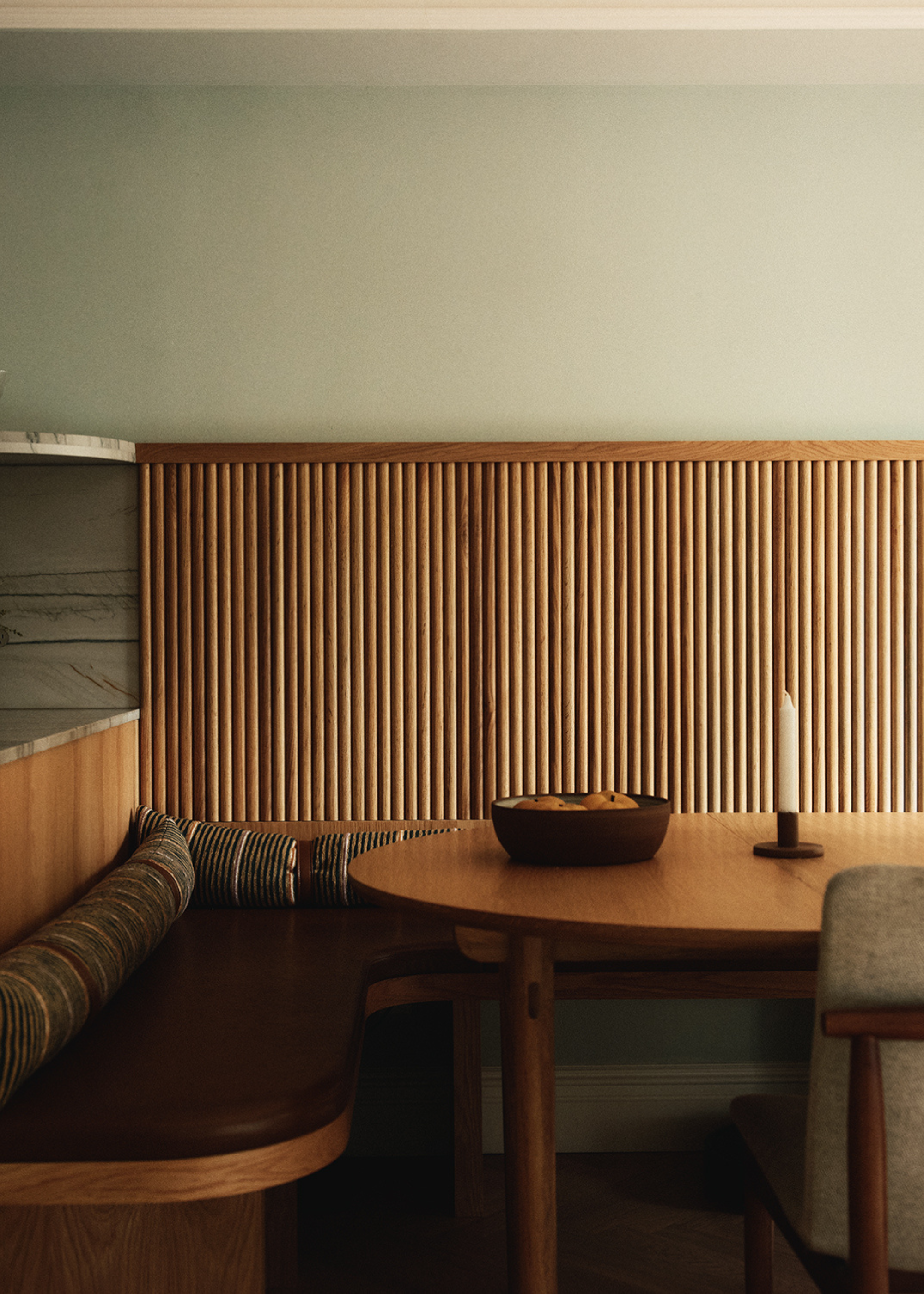 A dining room with banquette seating, a wood panelled accent wall, and striped bolster pillows