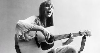 Joni Mitchell sitting cross-legged with her Martin acoustic