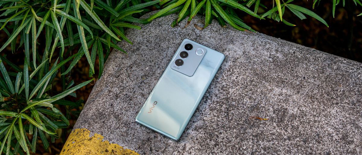 Vivo V27 lying face down on a cemented block surrounded by leaves