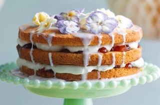 A three tiered elderflower drizzle cake topped with edible flowers and drizzled icing