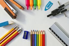Arrangement of stationary supplies including compass, ruler, colored pencils, sharpener, pencils, eraser, stapler, highlighters and paper clip on white background.