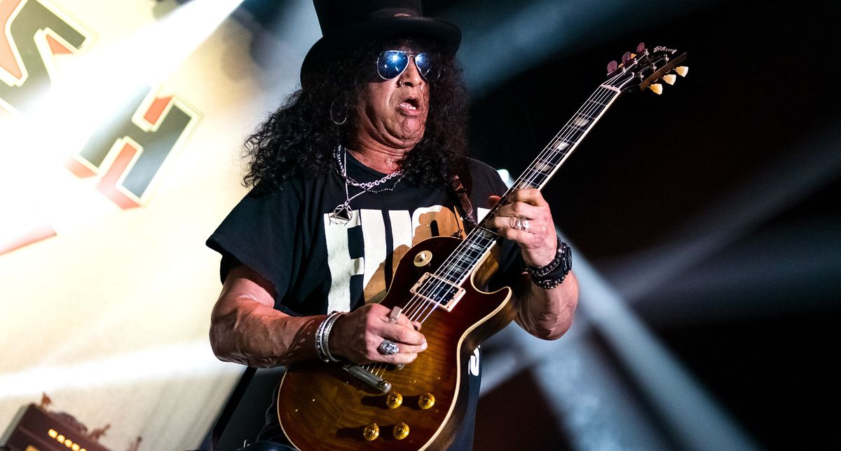 Slash plays a Gibson Les Paul onstage, against a backdrop of white stage lights