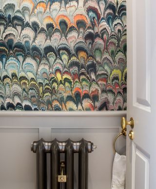 A powder room with multicolored patterned wallpaper, a small black radiator and a white hand towel