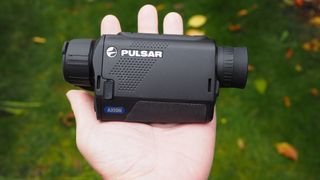 Pulsar Axion XQ30 PRO night vision monocular held in a hand outdoor over green grass