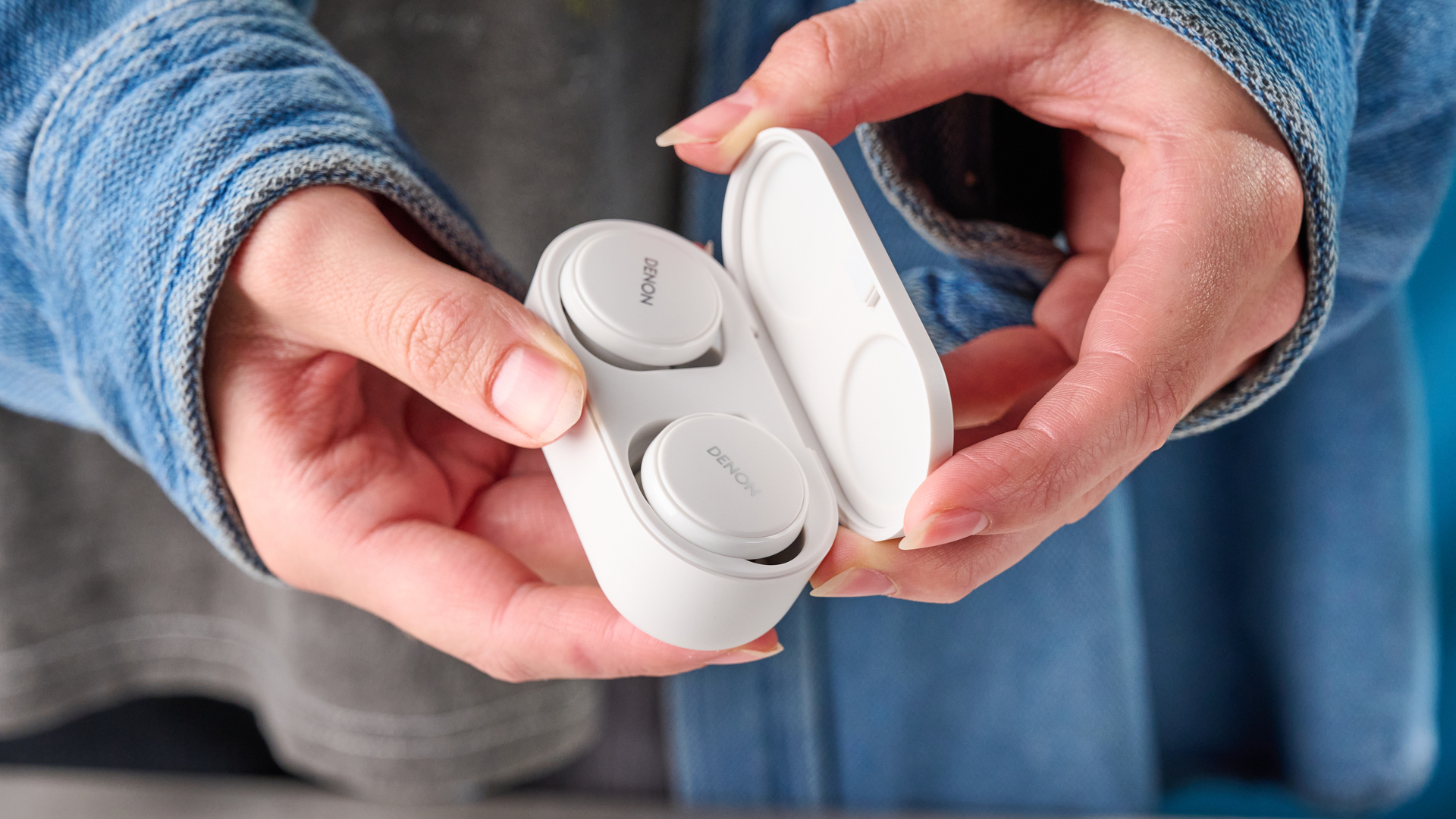 the denon perL Pro wireless earbuds in white, with circular earbud shapes, and a white charging case, photographed against a blue background