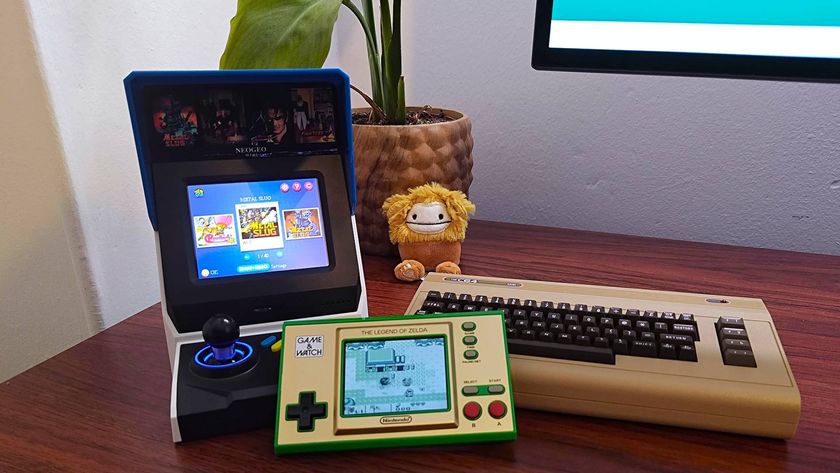 Neo Geo Mini on left, C64 mini on right, and Zelda: Game and Watch in centre on woodgrain desk with plant in backdrop next to Big Foot Squishmallow.