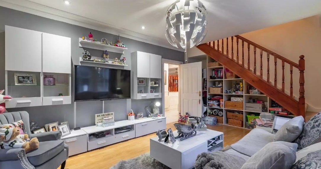 The bottom floor living room has a wall mounted tv and corner sofa with wooden staircase leading upstairs