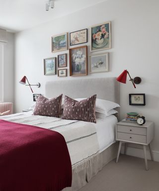 neutral bedroom with maroon throw and cushions, red wall lights and gallery wall