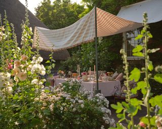 A table set under a fabric canopy propped on stilts in a cottage garden