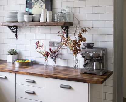 A coffee bar in a kitchen with wooden countertops, a steel coffee machine, and open shelving with plates and bowls