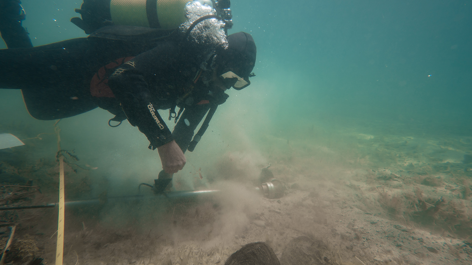 A diver carries an excavation tool near the bottom of the lake.