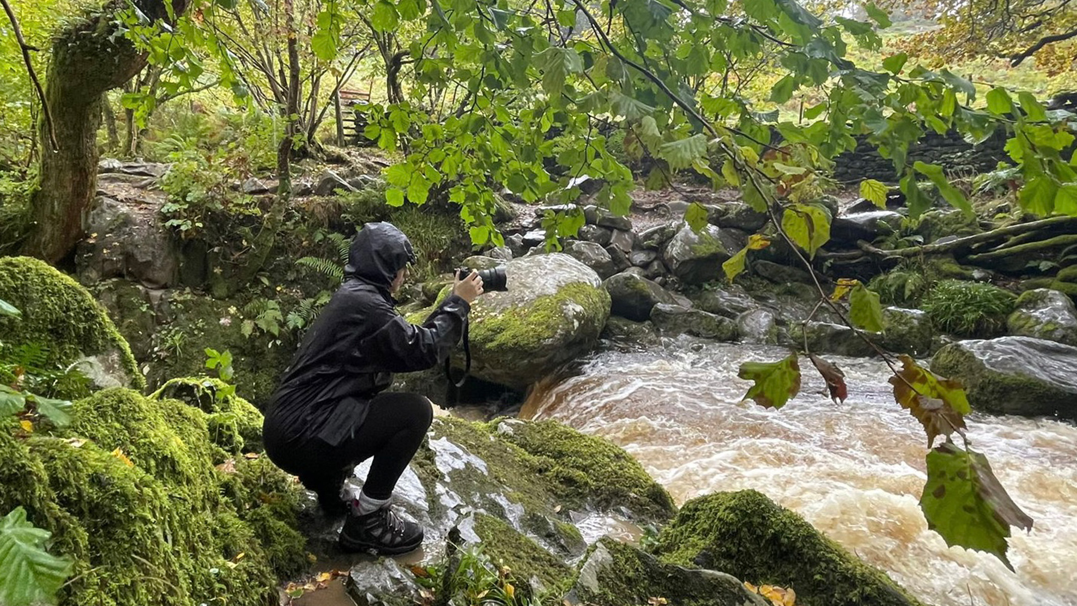Image shows a woman wearing waterproofs taking photos with the Sony A1.