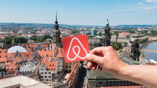 The Airbnb logo with a city in the background