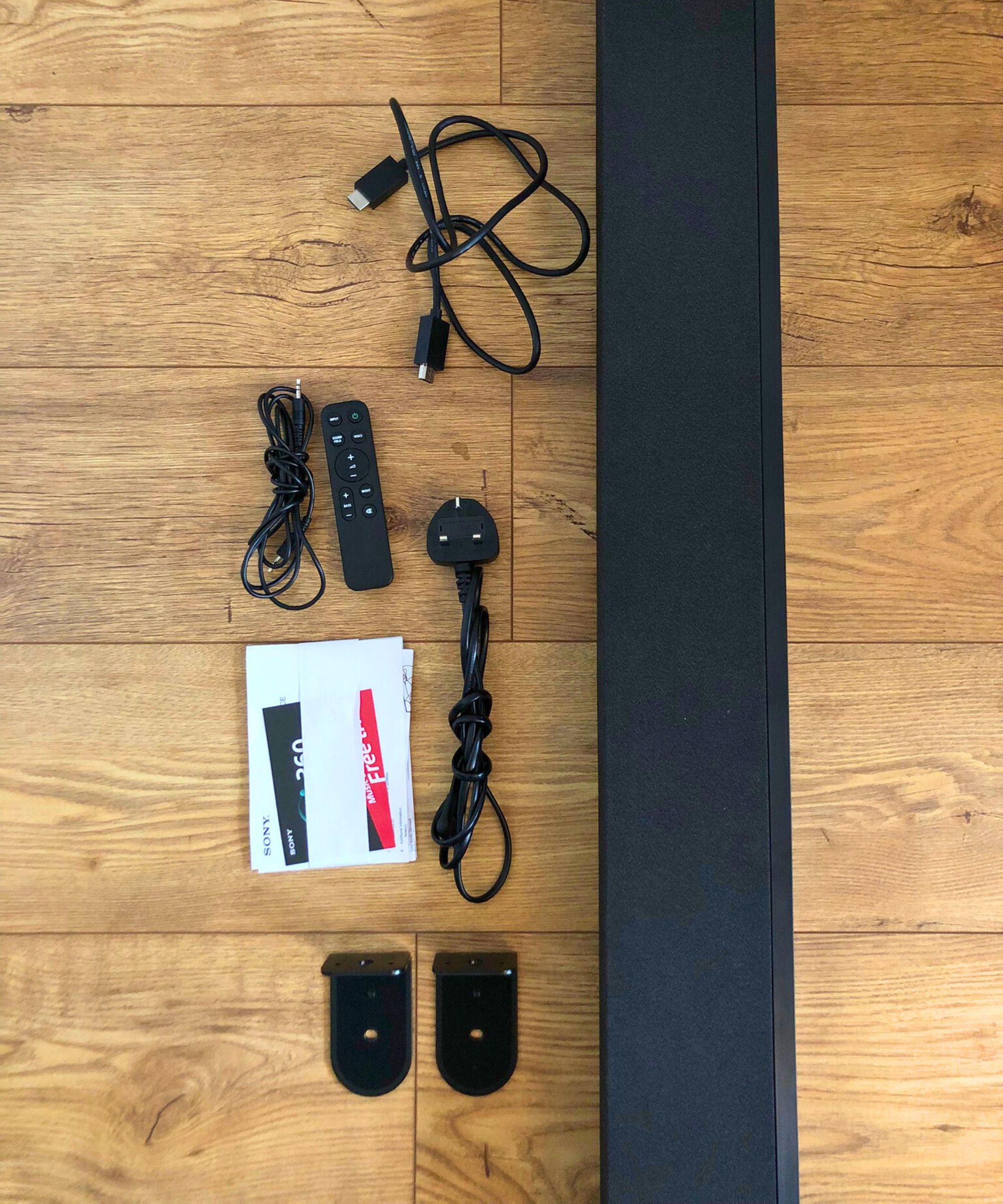 Cables, remote, manual and soundbar included as part of Sony BRAVIA Theater Bar 8, laid out on wooden floor in Dan Fauzi&#039;s home.