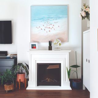 A white living room with a matching fireplace, an artwork hanging above it and houseplants surrounding it