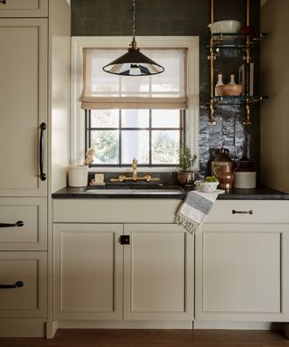 Kitchen sink with neutral cabinets and black zellige tiles on the wall