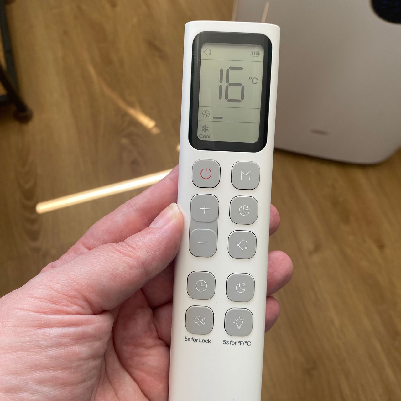 Hand holding the remote control of the Dreo 318s portable air conditioner
