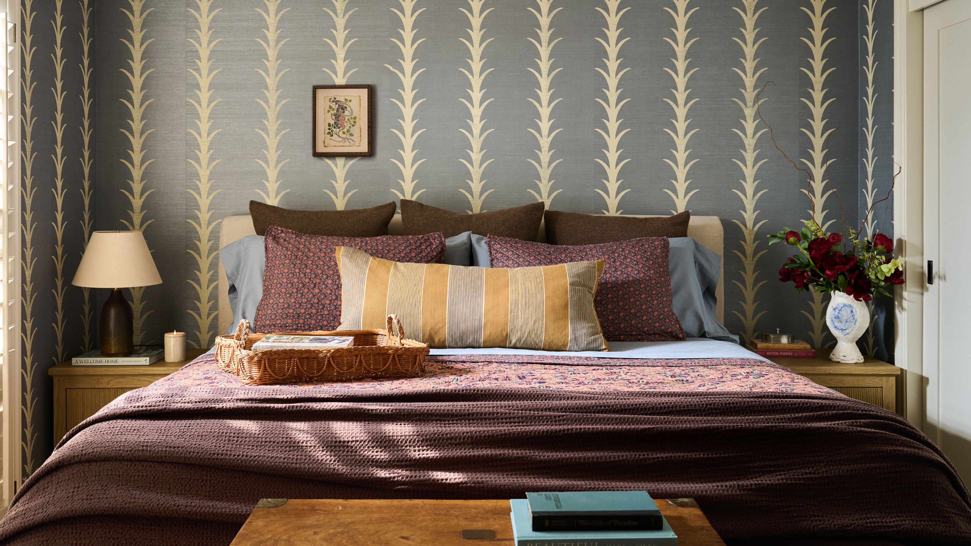 a soft blue wallpapered bedroom with purple and chocolate brown bed linens