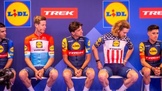 Three riders from Lidl-Trek sit on stage showing off their new kit