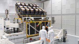 three men in clean room suits look at a spacecraft under assembly