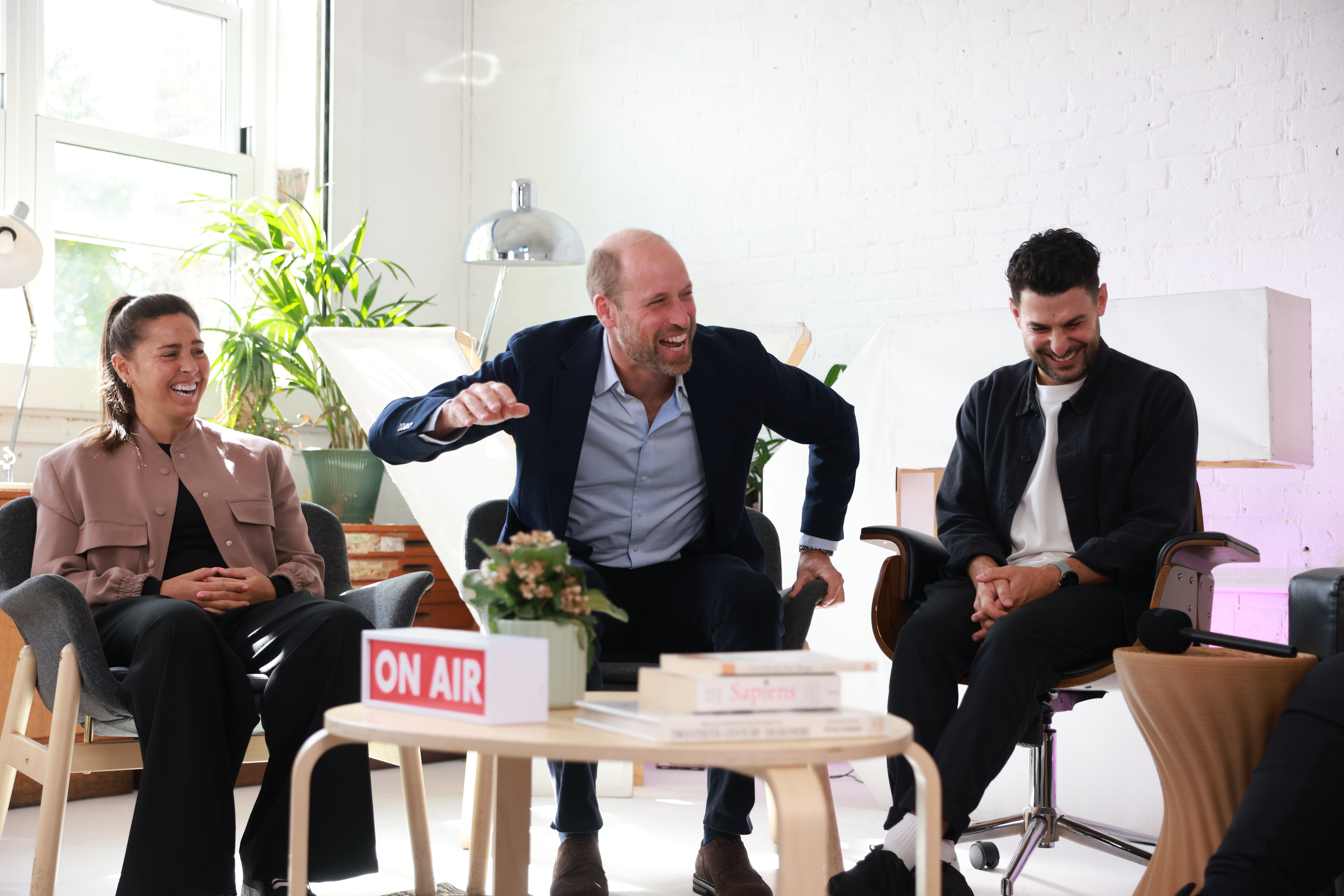 Prince William sitting in a chair and laughing with Fara Williams and a man