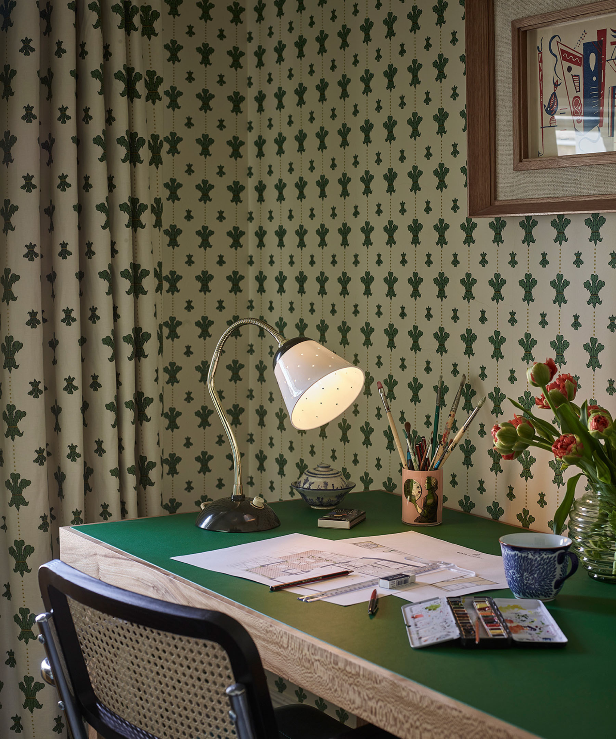 a workspace in a room with printed wallpaper and matching drapes, a small table lamp, and papers on the desk