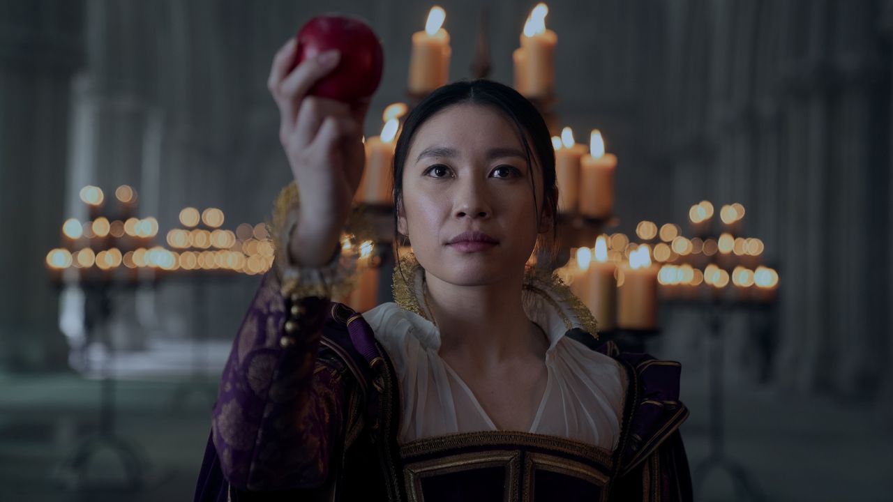 Jin Cheng (Jess Hong) holds up an apple while standing in front of an array of candles, in episode 103 of 3 Body Problem